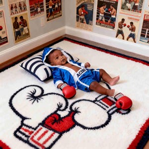 K&ouml;nnte beinhalten: Ein Baby in einem blauen Box-Outfit, das auf einem wei&szlig;en Teppich mit Boxhandschuh-Design liegt. Das Baby tr&auml;gt rote Boxhandschuhe. Box-Poster schm&uuml;cken die Wand.