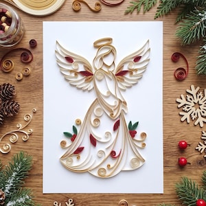May include: A paper quilling art piece on a white rectangular card featuring a stylised angel figure. The angel is constructed from coiled cream, gold, and dark red paper strips, forming wings, a halo, and a flowing gown with leaf accents.
