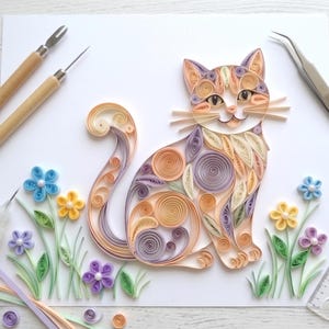 Op de afbeelding: Een kleurrijk papier quilling kunstwerk van een kat die tussen papieren bloemen zit. De kat is gemaakt van oranje, paarse en gele papieren stroken. De bloemen zijn blauw, geel en paars. Knutselgereedschap is zichtbaar.