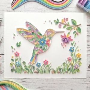 May include: A colorful paper quilling art piece featuring a hummingbird with outstretched wings, surrounded by flowers and greenery. The hummingbird is filled with intricate floral patterns in various colors. The artwork is on a white background.