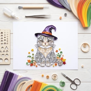 May include: A paper quilling art piece on white paper featuring a grey tabby cat wearing a purple witch hat with an orange band. The cat is surrounded by colorful paper quilled autumn leaves, small stars, and swirling green vine accents.