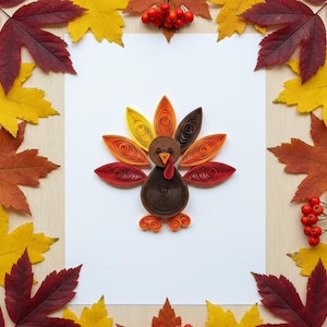 Könnte beinhalten: Eine Truthahn-Quilling-Figur mit rotem Kehllappen und orangefarbenem Schnabel sitzt auf weißem Hintergrund, umgeben von bunten Herbstblättern. Die Federn des Truthahns sind in Rot-, Orange- und Gelbtönen gehalten und schaffen ein festliches Herbstthema.