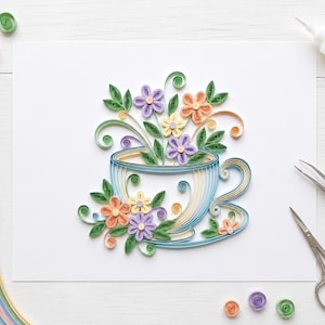 May include: A paper quilling art piece featuring a light blue teacup filled with colorful paper flowers and green leaves. The design includes purple, yellow, and orange blossoms with intricate swirls, surrounded by crafting tools like scissors, tweezers, and glue.