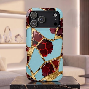 May include: A smartphone case featuring a geometric mosaic pattern of light blue and deep red segments separated by textured gold lines. The case has a black camera module cutout at the top with three circular lenses and a small flash aperture.