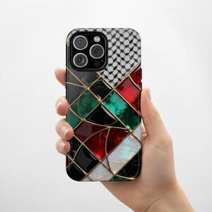 May include: A smartphone case with a geometric design in red, green, black, and white, framed by gold lines. The top right corner features a black and white checkered pattern. The case is held in a hand.