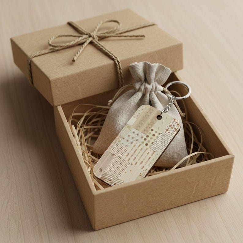 May include: A gift box with a decorative keychain and a small drawstring bag. The box is brown and tied with twine. The keychain has a patterned design in shades of beige and brown.