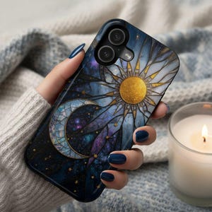 May include: A phone case featuring a celestial design with a gold sun, crescent moon, and stars against a dark blue and purple background. The case has a glossy finish and a black border. The design resembles stained glass.