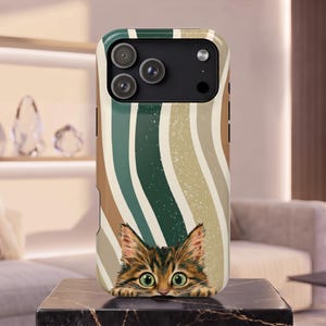 Peut inclure: Une coque de téléphone illustrée d'un chaton tigré brun dépassant du bord inférieur. Le fond présente des rayures verticales ondulées dans des tons vert foncé, beige et brun clair, avec une texture finement mouchetée sur l'ensemble.