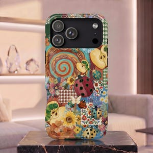 Pode incluir: Uma capa de smartphone com um design de colagem colorido com ilustrações de joaninhas, lagartas verdes, maçãs fatiadas, girassóis e vários padrões florais. A capa tem um módulo de câmara preto no topo com três lentes.