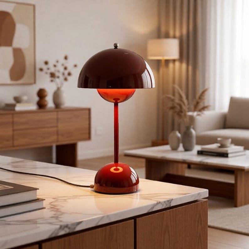 K&ouml;nnte beinhalten: Eine moderne, rote Tischlampe mit einem kuppelf&ouml;rmigen Schirm und einem schlanken Stiel. Die Lampe hat eine gl&auml;nzende Oberfl&auml;che und steht auf einer Marmorarbeitsplatte. Das Design ist minimalistisch und stilvoll, geeignet f&uuml;r die Inneneinrichtung.