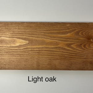 K&ouml;nnte beinhalten: Nahaufnahme einer hellen Eichenholzplanke mit sichtbarer Maserung und einem Astloch. Das Holz hat einen warmen, nat&uuml;rlichen Farbton und der Text "Light oak" wird unten angezeigt.