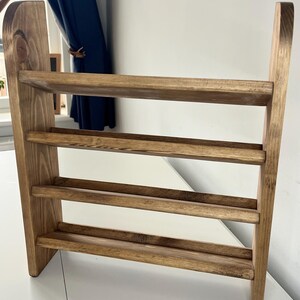 K&ouml;nnte beinhalten: Ein Schuhregal aus Holz mit drei Ablagen. Das Regal ist aus hellbraunem Holz gefertigt und hat ein schlichtes, minimalistisches Design. Die Ablagen werden von vertikalen Seitenteilen getragen.