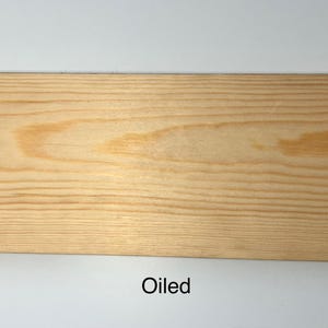K&ouml;nnte beinhalten: Nahaufnahme einer hellen, ge&ouml;lten Holzplanke. Die Holzmaserung ist sichtbar, mit Farbvariationen von hellem Beige bis zu einem dunkleren, w&auml;rmeren Ton. Das Wort "Oiled" ist unten im Bild in Schwarz gedruckt.