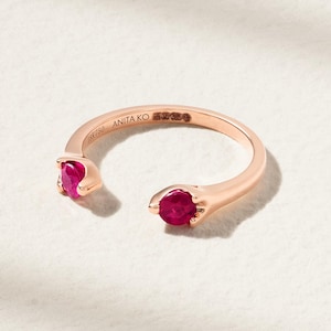 May include: Rose gold ring featuring two round, vibrant red gemstones. The ring is marked with "18k 750" and "ANITA KO". The design has a modern, open style, with the gemstones set at opposite ends of the band.