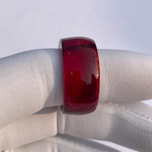 Puede incluir: Un vibrante anillo rojo translúcido. El anillo es una banda sólida con una superficie lisa y pulida. El color es un rojo intenso y rico, y el anillo parece estar hecho de un material sólido.