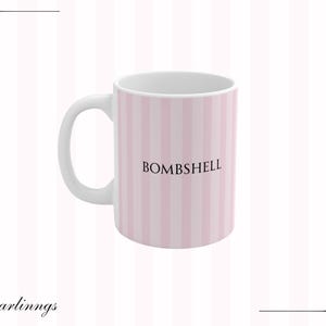 May include: White ceramic mug with a pink and white striped pattern. The word "BOMBSHELL" is printed in black on the side of the mug. The mug has a white handle and a white interior.