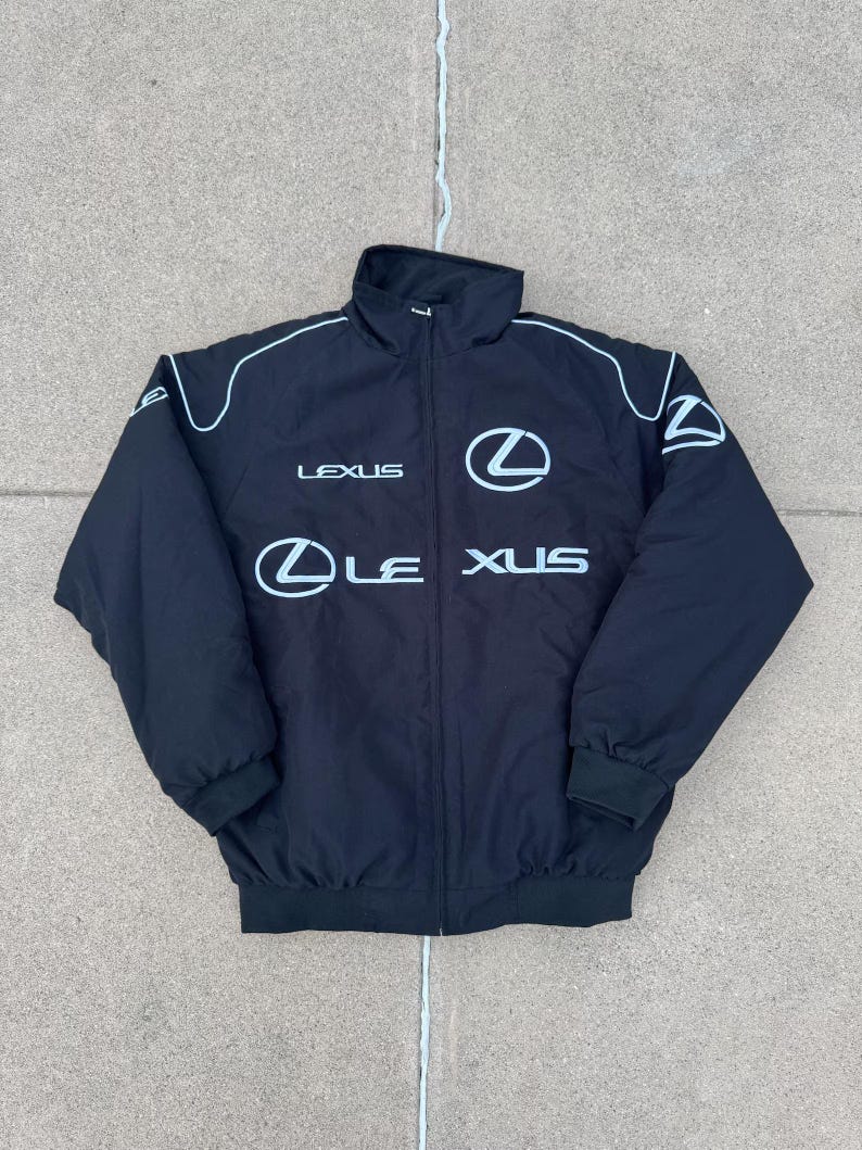 Pu&ograve; includere: Giacca nera con zip, profili bianchi e logo Lexus. La giacca ha un collo alto, polsini a coste e orlo a coste. Il logo Lexus &egrave; visualizzato sul petto e la parola "LEXUS" &egrave; stampata sopra il logo.