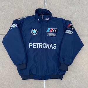 May include: Navy blue jacket with a full-length zipper and a stand-up collar. The jacket features the BMW logo, the word "Power", and the word "PETRONAS" in white. The sleeves have the word "wer" and "Credit Suisse" printed on them.
