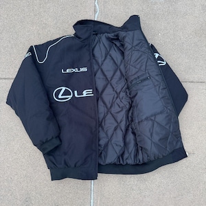 Pu&ograve; includere: Giacca nera con finiture bianche e logo Lexus sul petto. La giacca ha un interno trapuntato e una tasca con cerniera. Il colletto &egrave; a collo alto e la giacca ha orlo e polsini a coste.