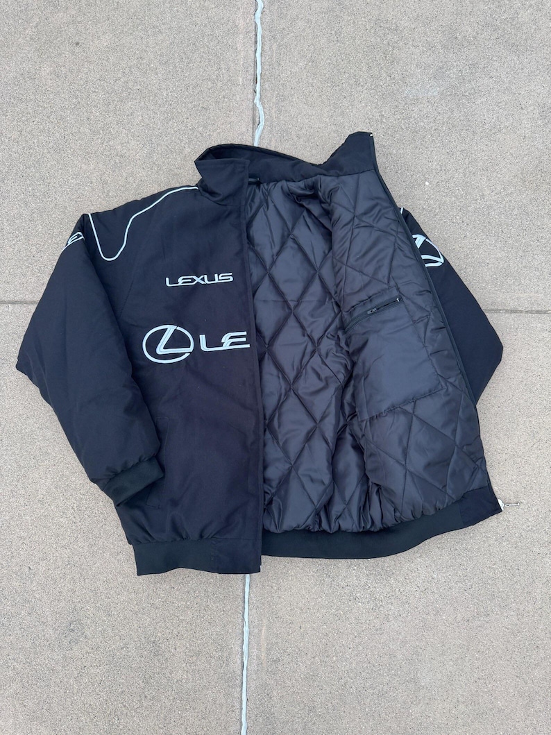 Pu&ograve; includere: Giacca nera con finiture bianche e logo Lexus sul petto. La giacca ha un interno trapuntato e una tasca con cerniera. Il colletto &egrave; a collo alto e la giacca ha orlo e polsini a coste.
