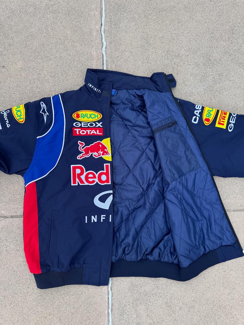May include: Navy blue racing jacket with red and white accents. Features multiple sponsor logos, including "Red Bull" and "Infiniti." The jacket has a quilted interior and a zip-up front.