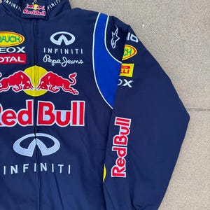 May include: Navy blue Red Bull racing jacket with multiple sponsor logos. Features the Red Bull logo, Infiniti, and Pepe Jeans branding. The jacket has a blue and white design on the sleeves and collar.