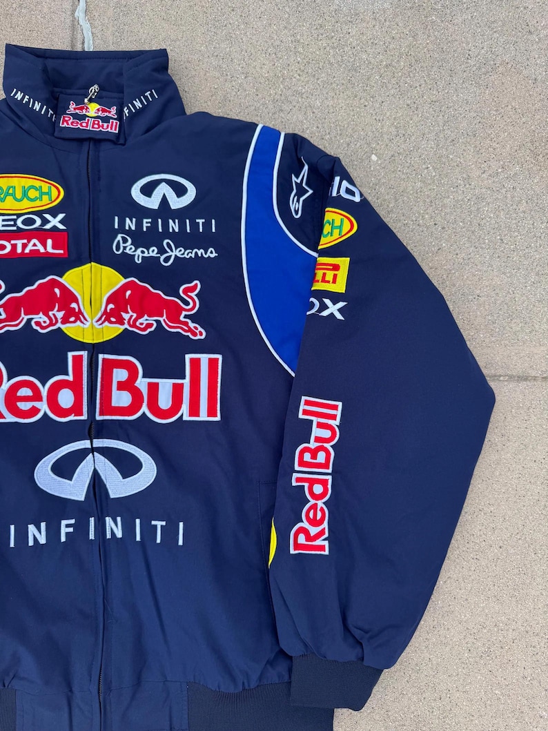 May include: Navy blue Red Bull racing jacket with multiple sponsor logos. Features the Red Bull logo, Infiniti, and Pepe Jeans branding. The jacket has a blue and white design on the sleeves and collar.