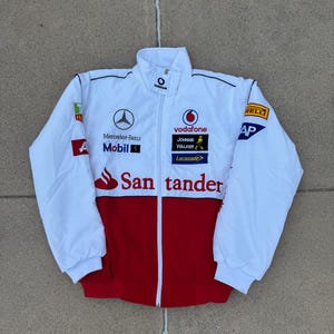 Puede incluir: Chaqueta de carreras blanca y roja con múltiples logotipos de patrocinadores, incluidos Vodafone, Mercedes-Benz y Santander. La chaqueta tiene una cremallera completa y un cuello alto. La chaqueta es de talla mediana.