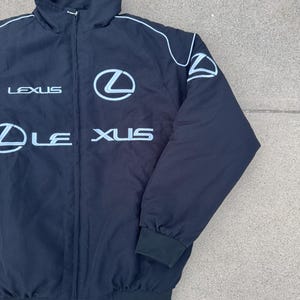 Pu&ograve; includere: Giacca nera con zip con loghi e testo Lexus bianchi. La giacca ha un collo alto, profili bianchi e polsini e orlo a coste neri. Il logo Lexus &egrave; ben visibile sul petto.