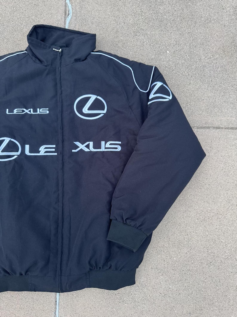 Pu&ograve; includere: Giacca nera con zip con loghi e testo Lexus bianchi. La giacca ha un collo alto, profili bianchi e polsini e orlo a coste neri. Il logo Lexus &egrave; ben visibile sul petto.