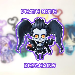 May include: A cartoon keychain featuring a character from Death Note, with black wings, spiky hair, and a sinister grin. The character holds a red apple. The text "DEATH NOTE KEYCHAINS" is displayed in purple.