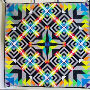 May include: A colorful quilt with a geometric pattern of black, white, gray, red, yellow, blue, and green triangles. The quilt is made up of repeating patterns of triangles that create a starburst effect in the center.