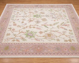 May include: Cream-colored rectangular rug with a floral pattern in shades of pink, green, and tan. The rug has a border with a repeating geometric design in a muted rose color. The floral design includes stylized flowers and leaves.