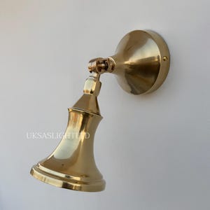 Peut inclure: Un luminaire mural en laiton poli avec une base ronde et une tête réglable. La lampe est fixée sur un mur blanc. Le texte "UKSASLIGHTLTD" est visible sur le luminaire. Idéal pour l'éclairage décoratif.