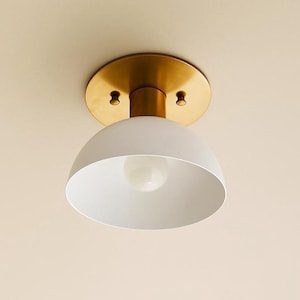 May include: A contemporary ceiling light fitting featuring a white, domed lampshade and a brass-toned mounting plate. The light bulb is visible within the shade. Designed for flush mounting.