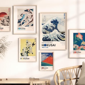 May include: A gallery wall set of six framed art prints featuring iconic works by Katsushika Hokusai, including The Great Wave off Kanagawa, red Mount Fuji, cranes, and floral motifs, all displayed in light wood frames with white matting.