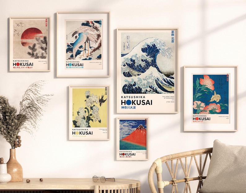 May include: A gallery wall set of six framed art prints featuring iconic works by Katsushika Hokusai, including The Great Wave off Kanagawa, red Mount Fuji, cranes, and floral motifs, all displayed in light wood frames with white matting.