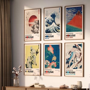 May include: A set of six framed wall art prints featuring Katsushika Hokusai artwork. Each vertical print displays a unique Japanese-inspired illustration, including a red sun, a large wave, a mountain, flowers, and birds, with bold text labels.