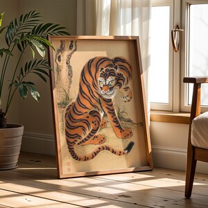 May include: A framed artwork featuring a stylized tiger with orange and black stripes. The tiger is depicted in a seated position with a detailed face and a long tail. The artwork is set against a beige background with a tree and grass.