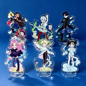 May include: Six clear acrylic standees featuring anime-style characters in various outfits and poses. The figures include a person with long brown hair, a guitarist with white hair, a person in a black coat, a person with pink hair, a person in white, and a person in a light blue outfit.