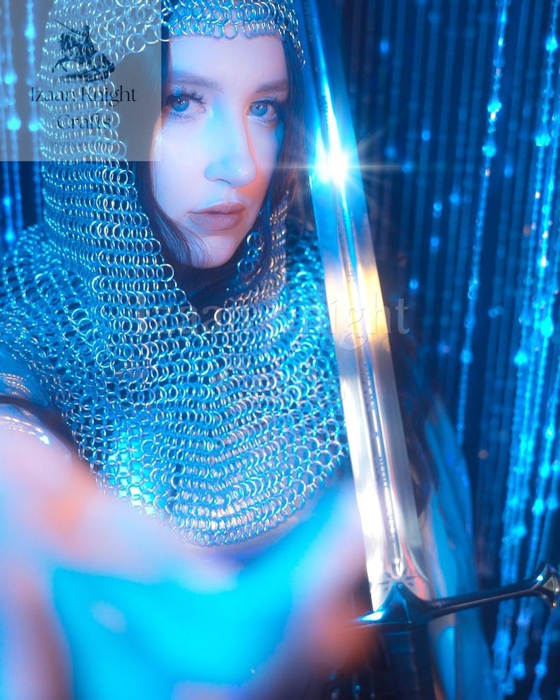 May include: A person wearing a chainmail hood and holding a sword. The sword is silver with a detailed hilt. The image has a blue and white colour scheme, with the text "Izaar Knight Crafts" visible in the upper left corner.