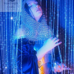 May include: A person wearing a silver chainmail hood and a gold breastplate, with a dark blue cloak. The image is illuminated with blue light and features the text "Izaan Knight Crafts".