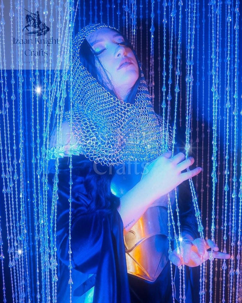 May include: A person wearing a silver chainmail hood and a gold breastplate, with a dark blue cloak. The image is illuminated with blue light and features the text "Izaan Knight Crafts".