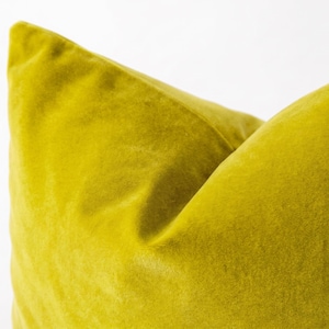 May include: A square throw pillow cover made of a solid chartreuse yellow velvet fabric. The material features a soft, short-pile texture with visible light reflection and shadows that create depth across the surface of the cushion.