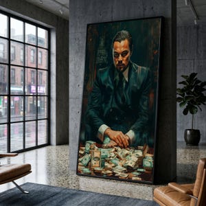 May include: A framed wall art print depicting a man in a dark suit sitting at a desk covered in stacks of United States dollar bills. The man has dark hair and a serious expression, with his hands clasped together resting on the pile of currency.