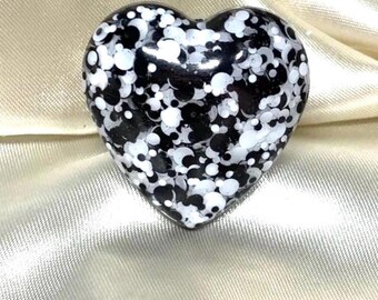 Può includere: Un oggetto decorativo a forma di cuore con finitura lucida. La superficie è ricoperta da un motivo a pois bianchi e neri. L'oggetto è appoggiato su un tessuto di raso.