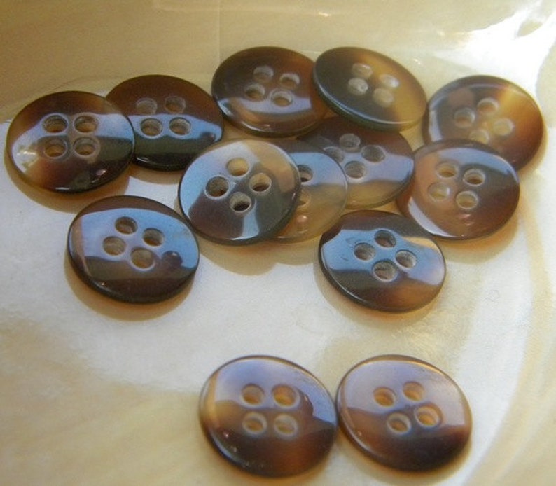May include: A collection of brown and black four-hole buttons. The buttons are made of a shiny material and have a slightly iridescent sheen.