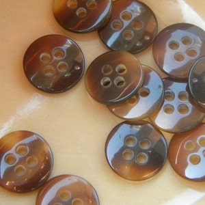 May include: A collection of brown, round buttons with four holes each. The buttons have a glossy finish and are arranged in a random pattern.