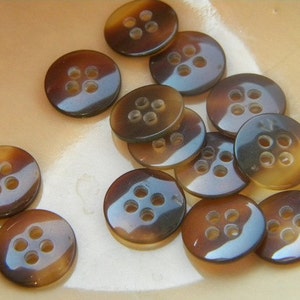 May include: A collection of brown and black buttons with four holes each. The buttons are arranged in a bowl.