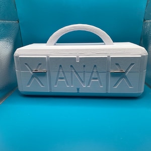 May include: A white, rectangular box with a handle on top and the word "XANAX" printed on the front. The box is sitting on a blue surface. The handle is arched and the box has a textured appearance.